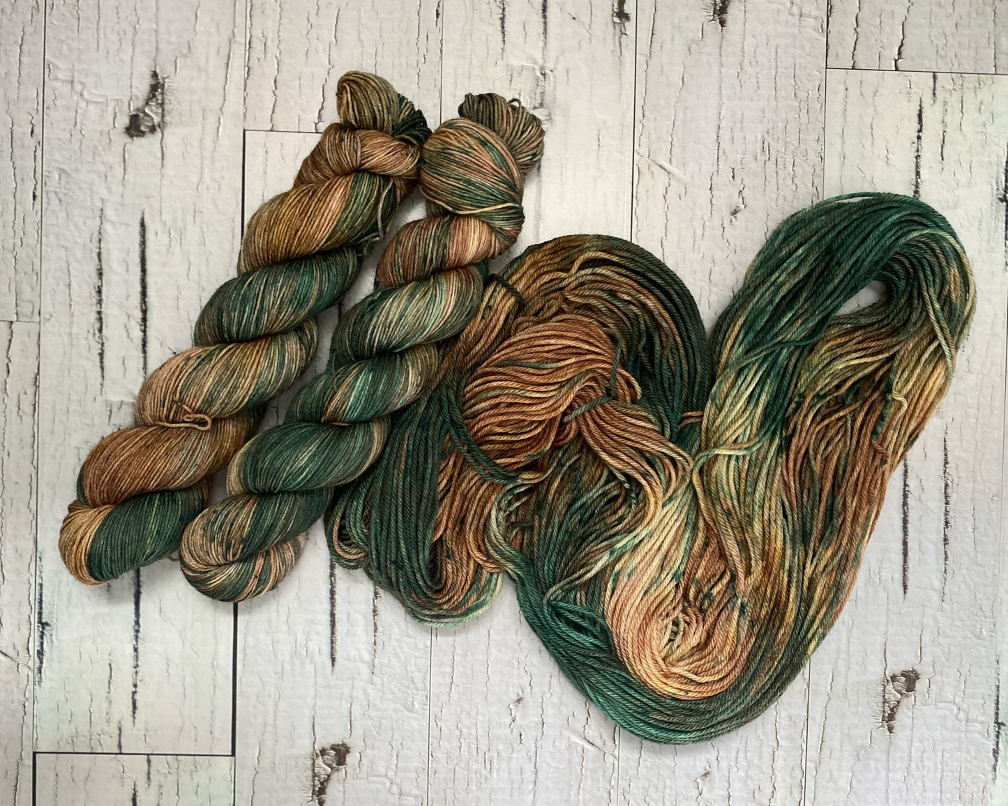 Two skeins of brown and green variegated yarn with a third hank of yarn laid out beside them. 