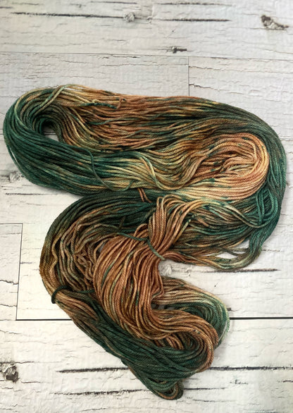 A hank of  variegated hand dyed yarn laid out on a white wood board background. The yarn consists of beautiful fawn brown and forest green tones.