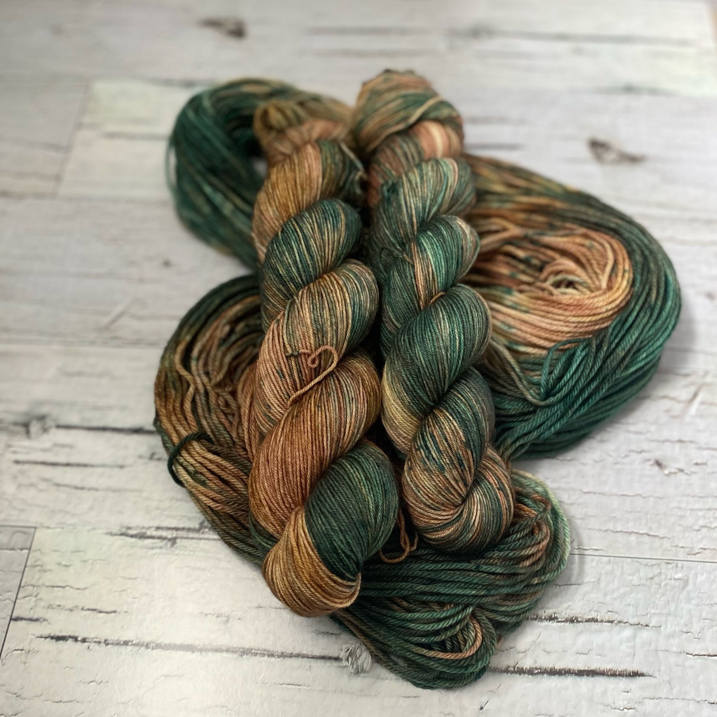 Two skeins of brown and green variegated yarn on a third hank of yarn laid out underneath them. 