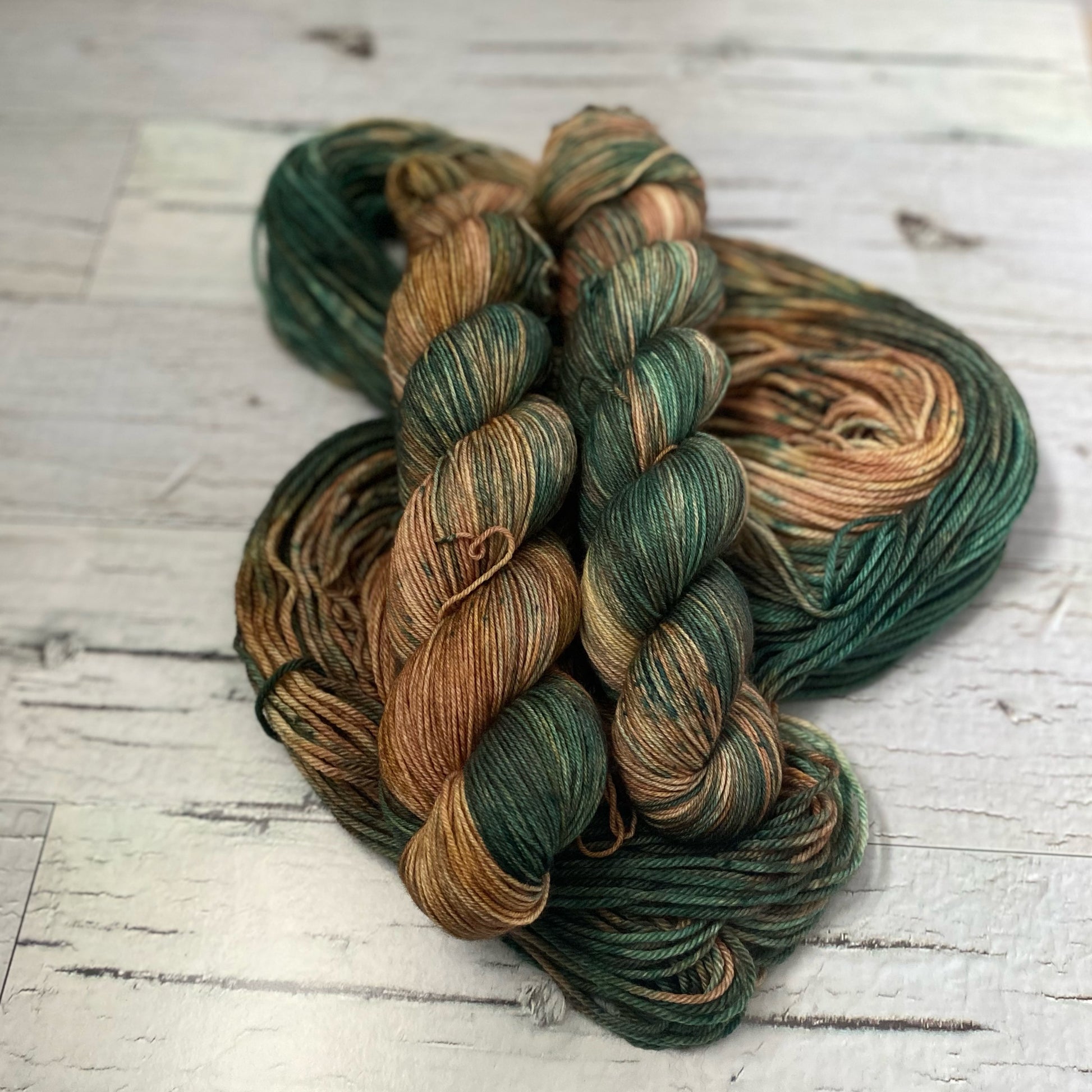 Two skeins of brown and green variegated yarn on a third hank of yarn laid out underneath them. 