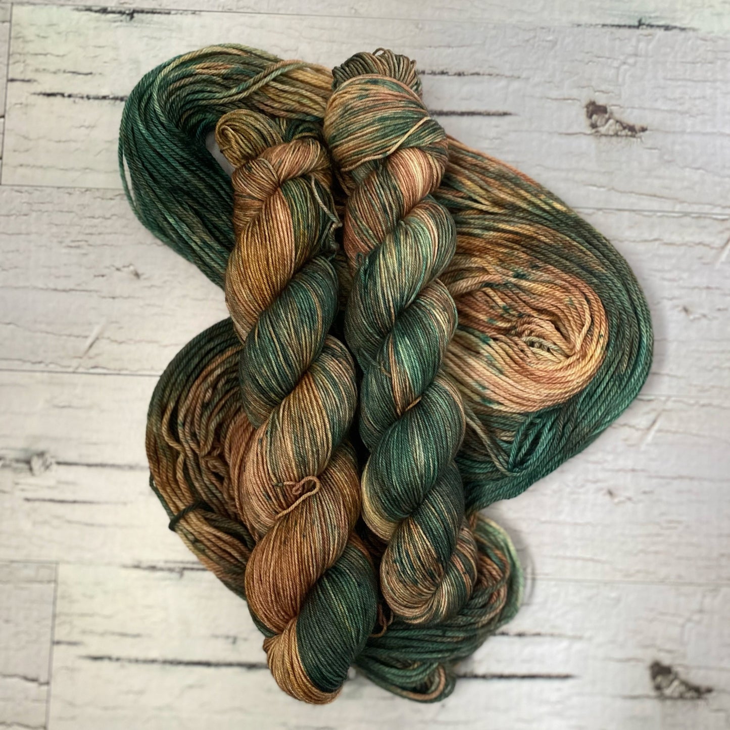 Two skeins of brown and green variegated yarn on a third hank of yarn laid out underneath them. 