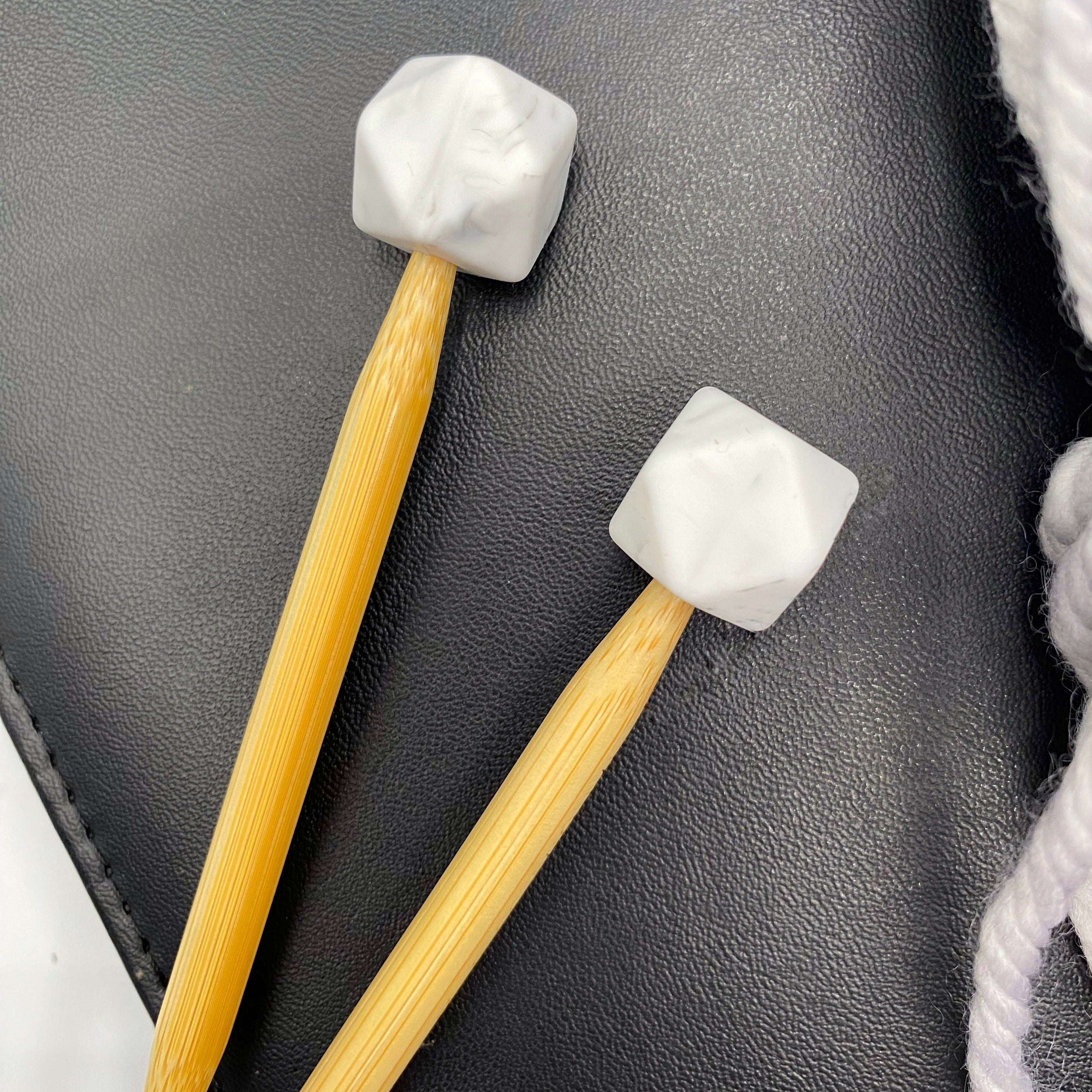 a set of knitting needles adorned with marbled hexagon point protectors, laid on top of a faux leather needle case.