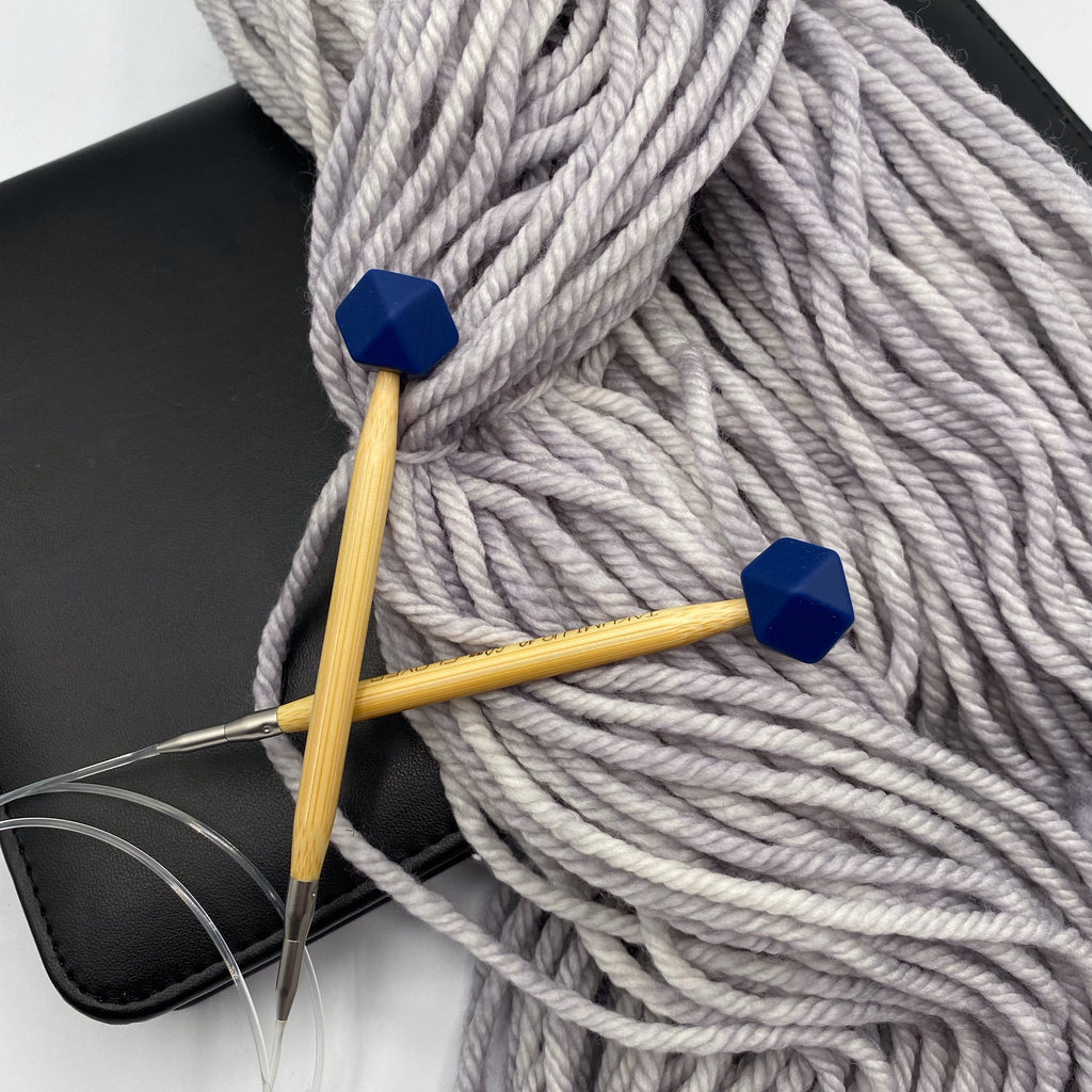 a set of knitting needles adorned with navy hexagon point protectors, laid on top of our Everyday Bulky in Urban.