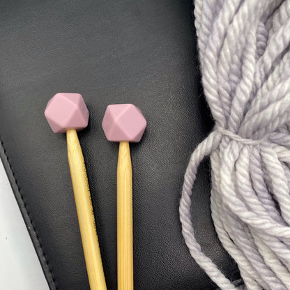 a set of knitting needles adorned with mauve hexagon point protectors, laid on top of a faux leather needle case, beside our Everyday Bulky in Urban.