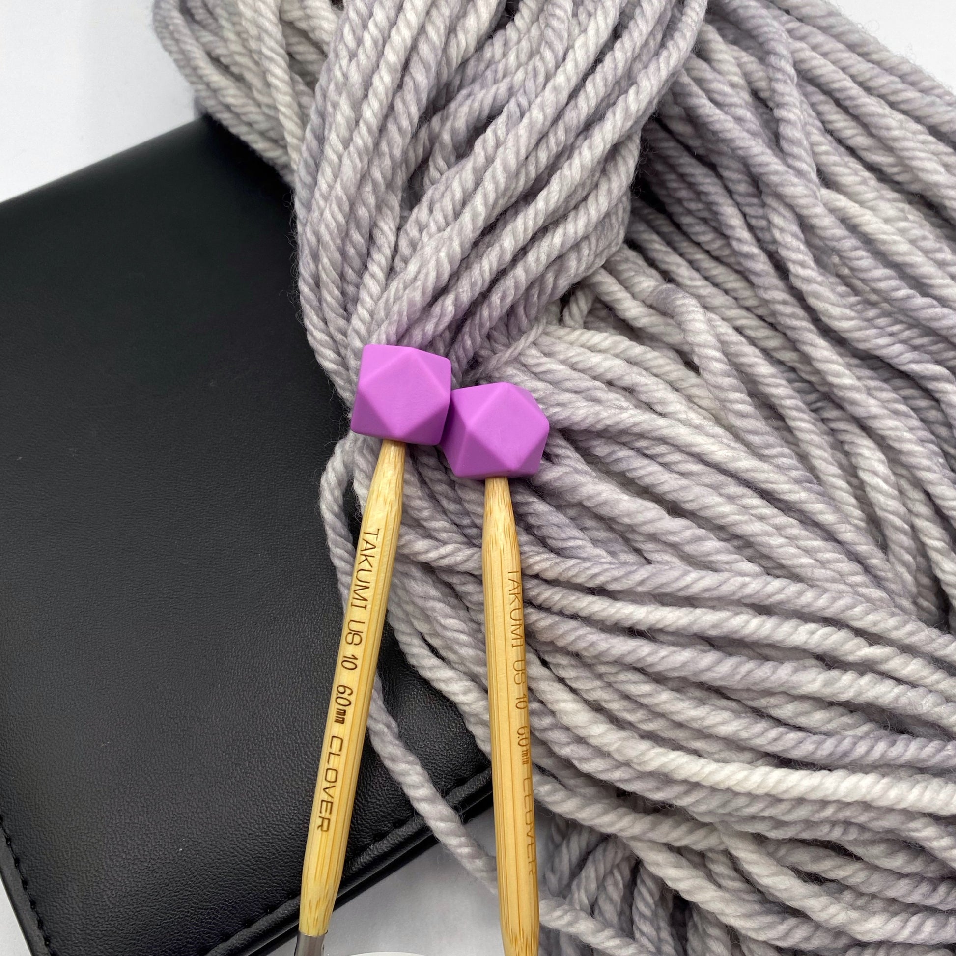 a set of knitting needles adorned with orchid (purple) hexagon point protectors, laid on top of our Everyday Bulky in Urban.