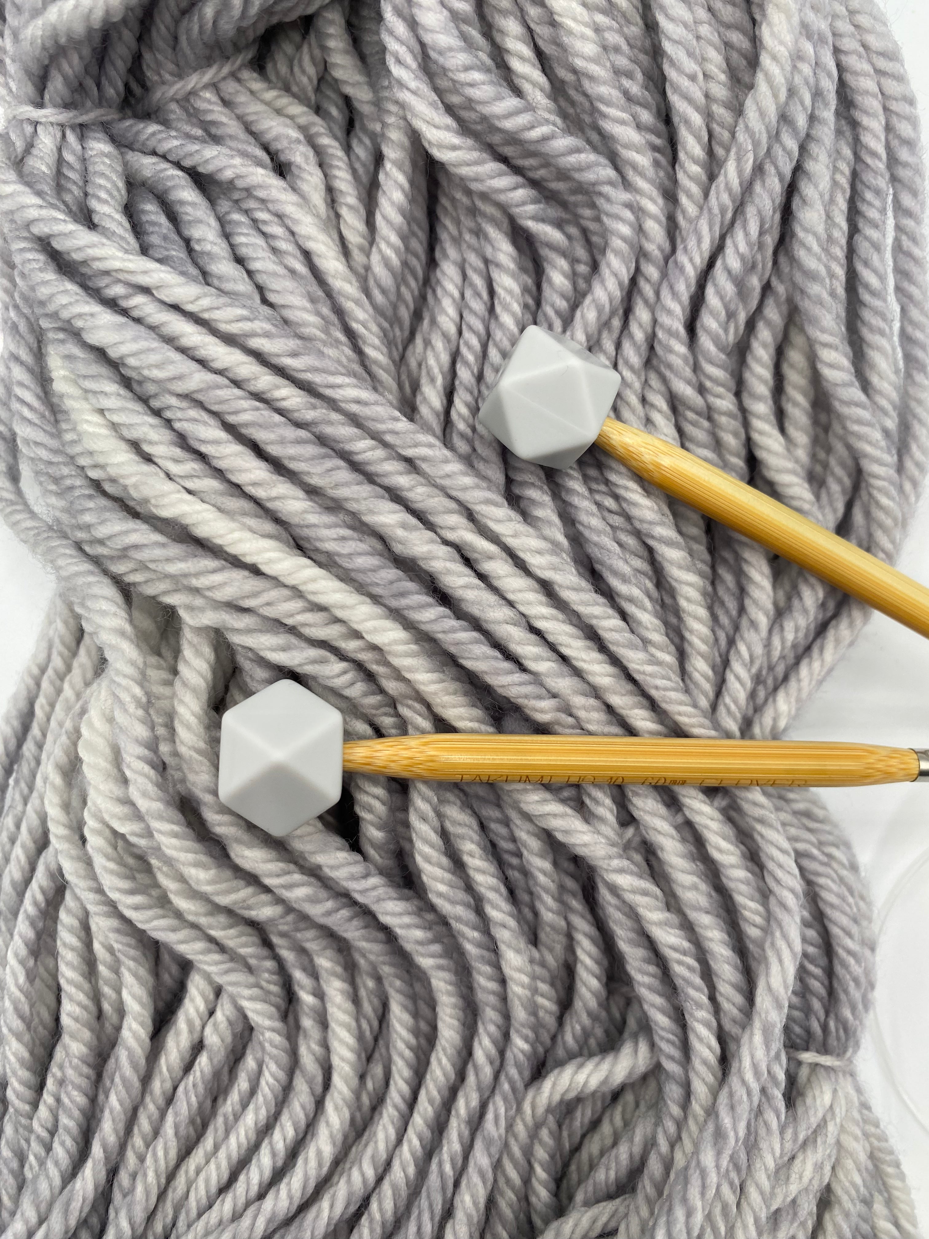 a set of knitting needles adorned with overcast (grey) hexagon point protectors, laid on top of our Everyday Bulky in Urban.