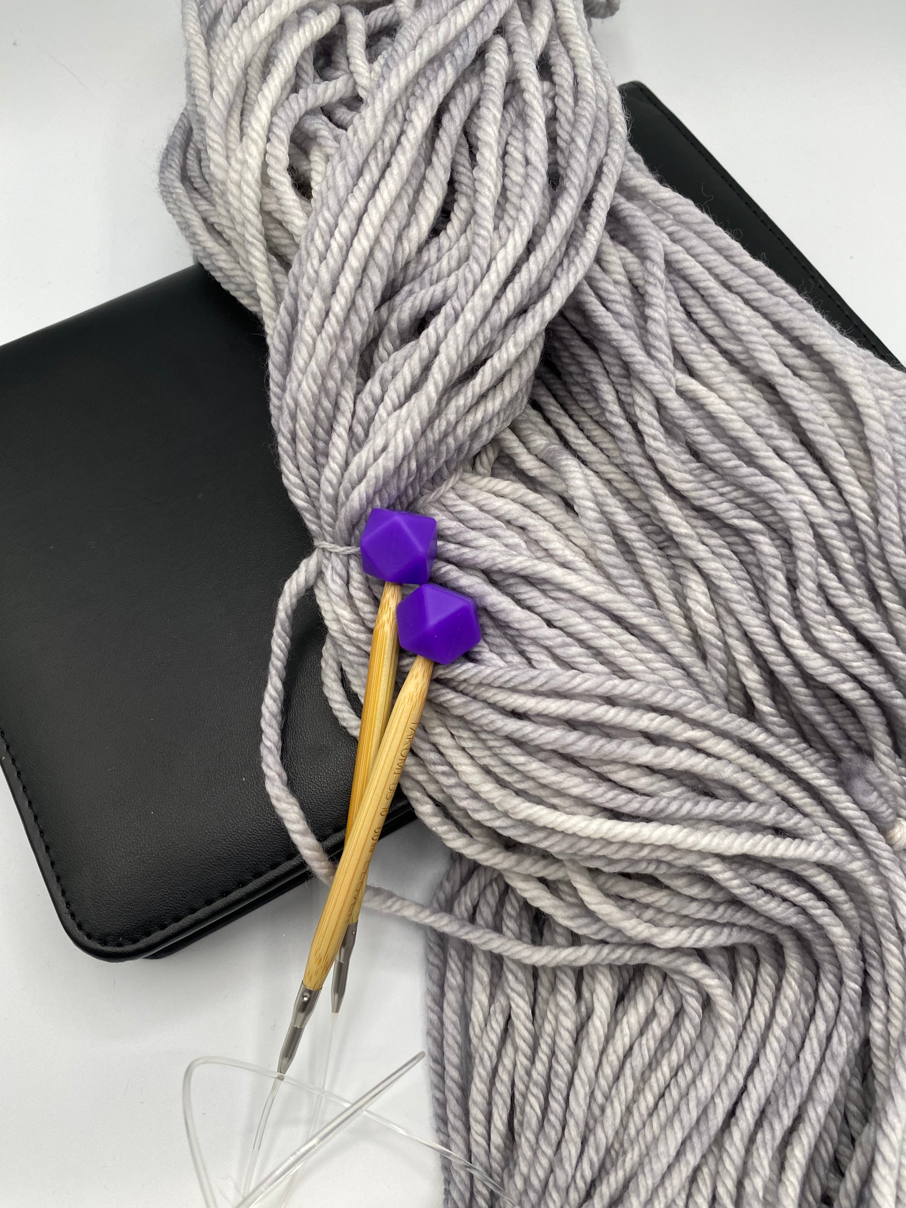 a set of knitting needles adorned with purple hexagon point protectors, laid on top of our Everyday Bulky in Urban.