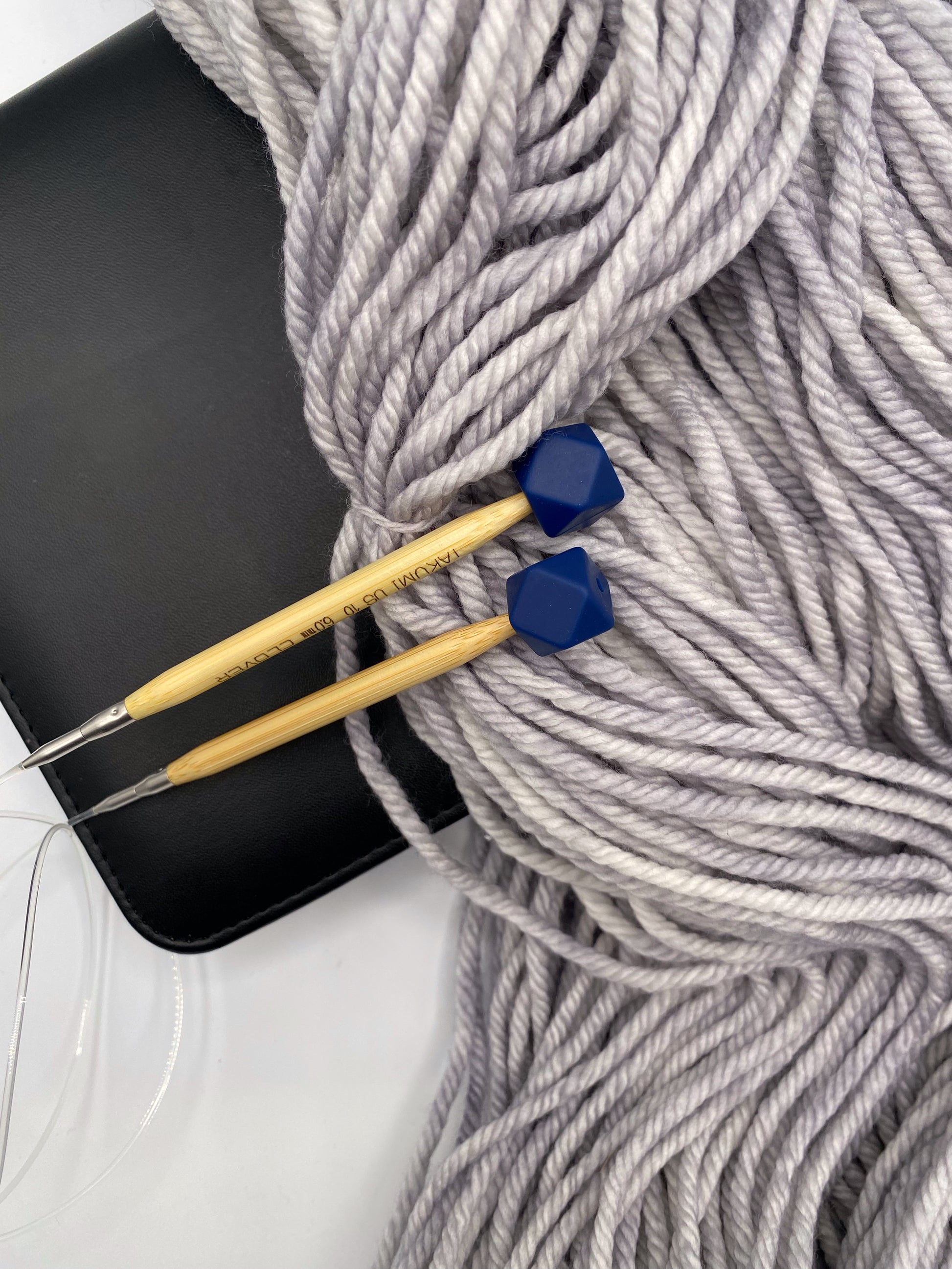a set of knitting needles adorned with navy hexagon point protectors, laid on top of a spread of our Everyday Bulky in Urban.