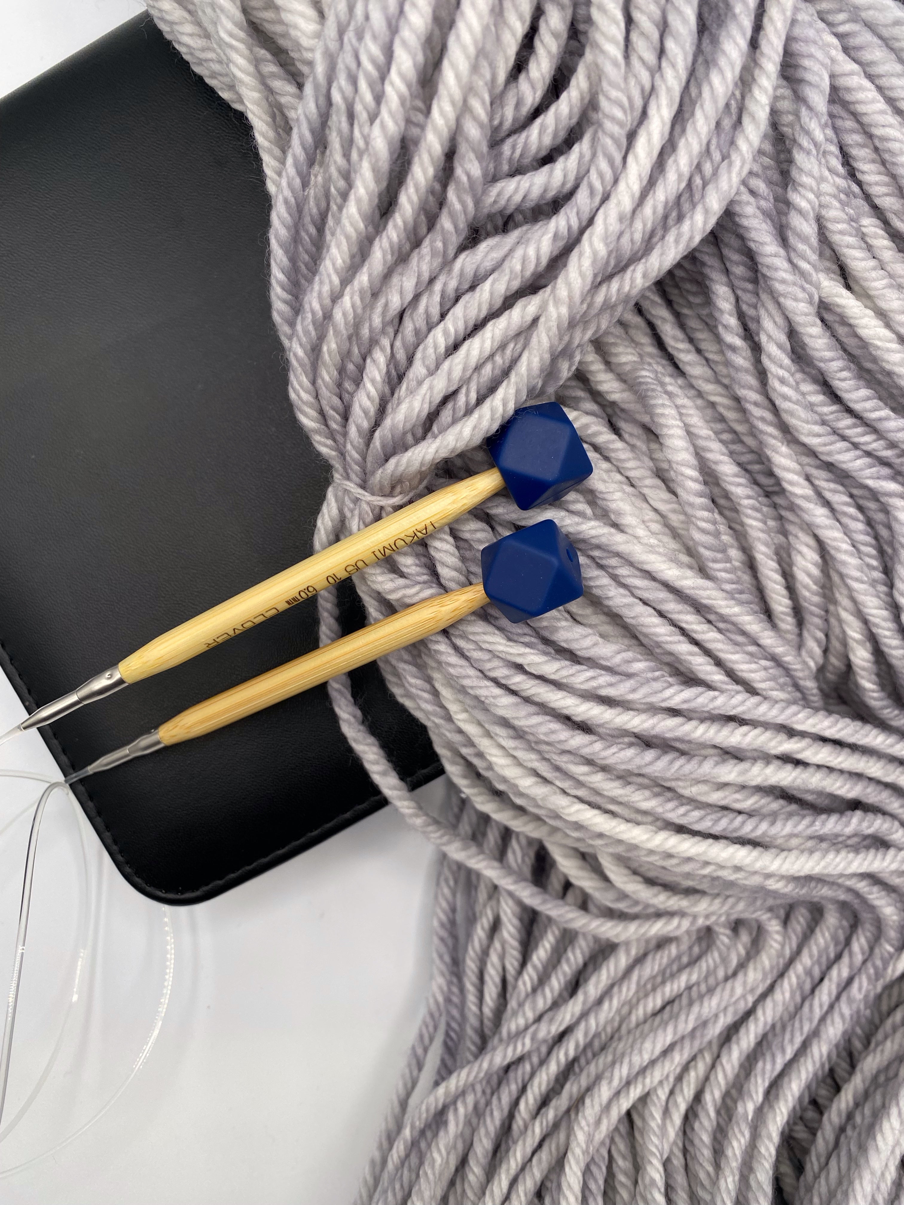 a set of knitting needles adorned with navy hexagon point protectors, laid on top of a spread of our Everyday Bulky in Urban.