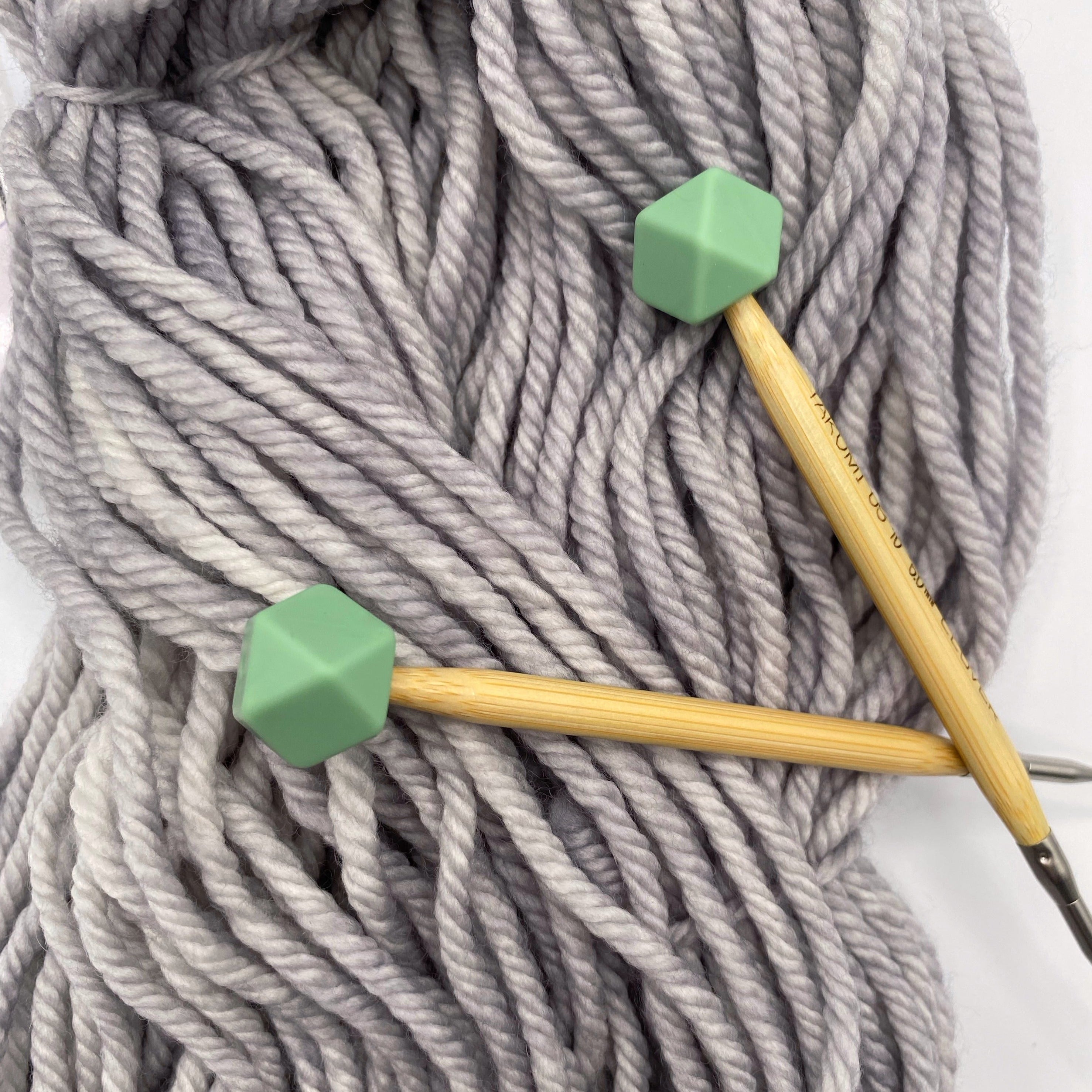 a set of knitting needles adorned with sage hexagon point protectors, laid on top of a spread of our Everyday Bulky in Urban.