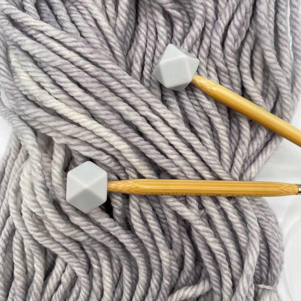 a set of knitting needles adorned with overcast (grey) hexagon point protectors, laid on top of our Everyday Bulky in Urban.
