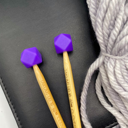 a set of knitting needles adorned with charcoal hexagon point protectors, laid on top of a faux leather needle case, beside our Everyday Bulky in Urban.