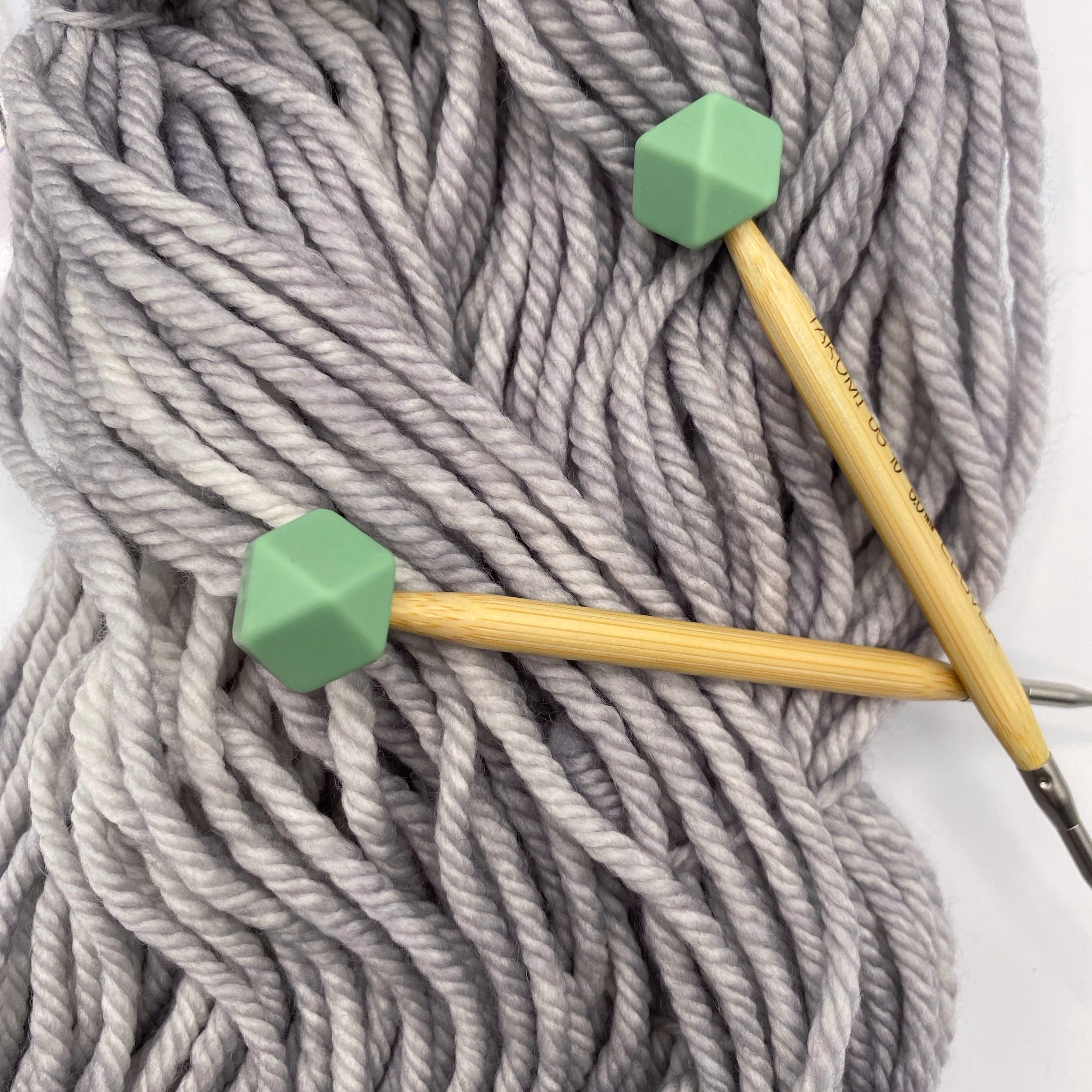 a set of knitting needles adorned with sage hexagon point protectors, laid on top of our Everyday Bulky in Urban.