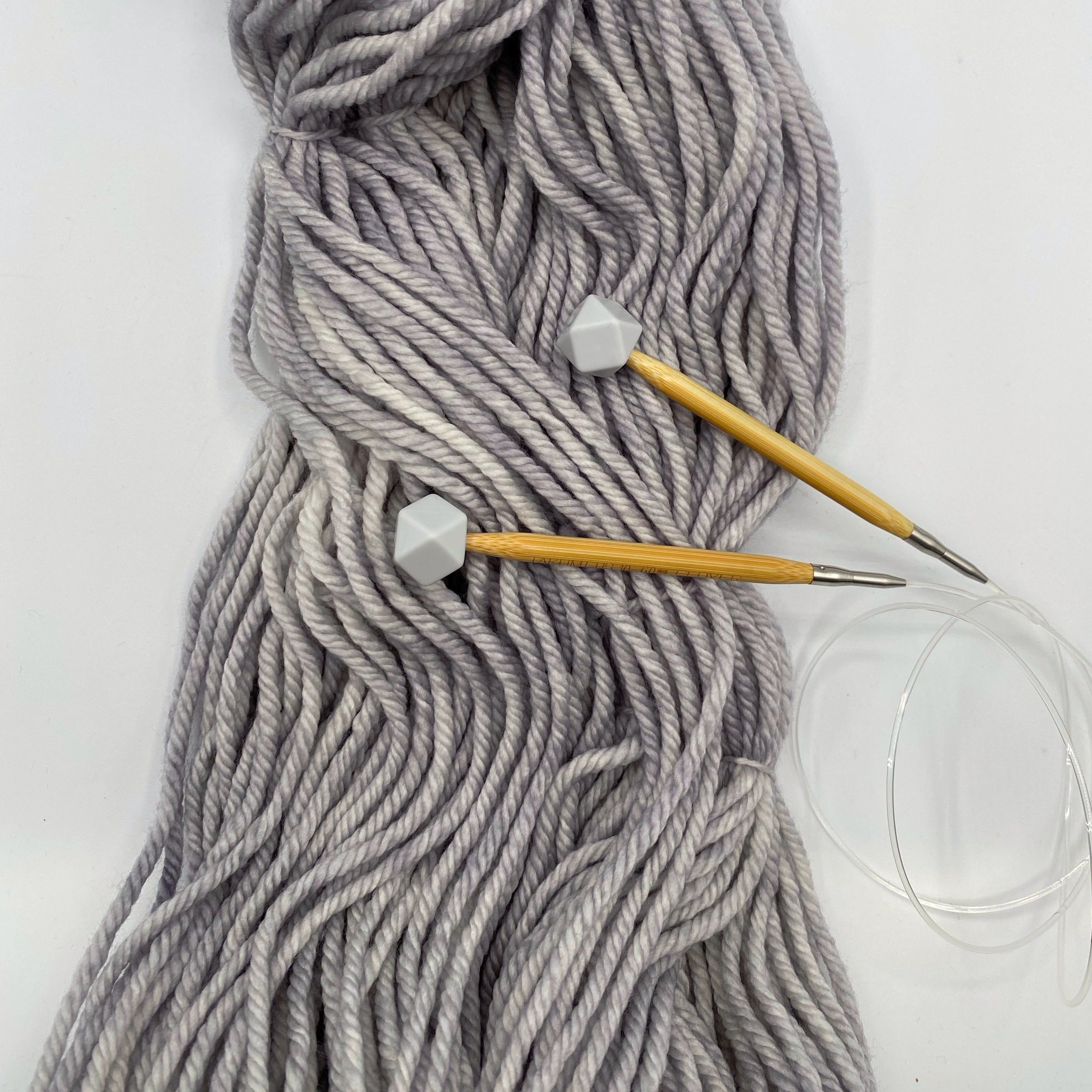 a set of knitting needles adorned with overcast (grey) hexagon point protectors, laid on top of our Everyday Bulky in Urban.