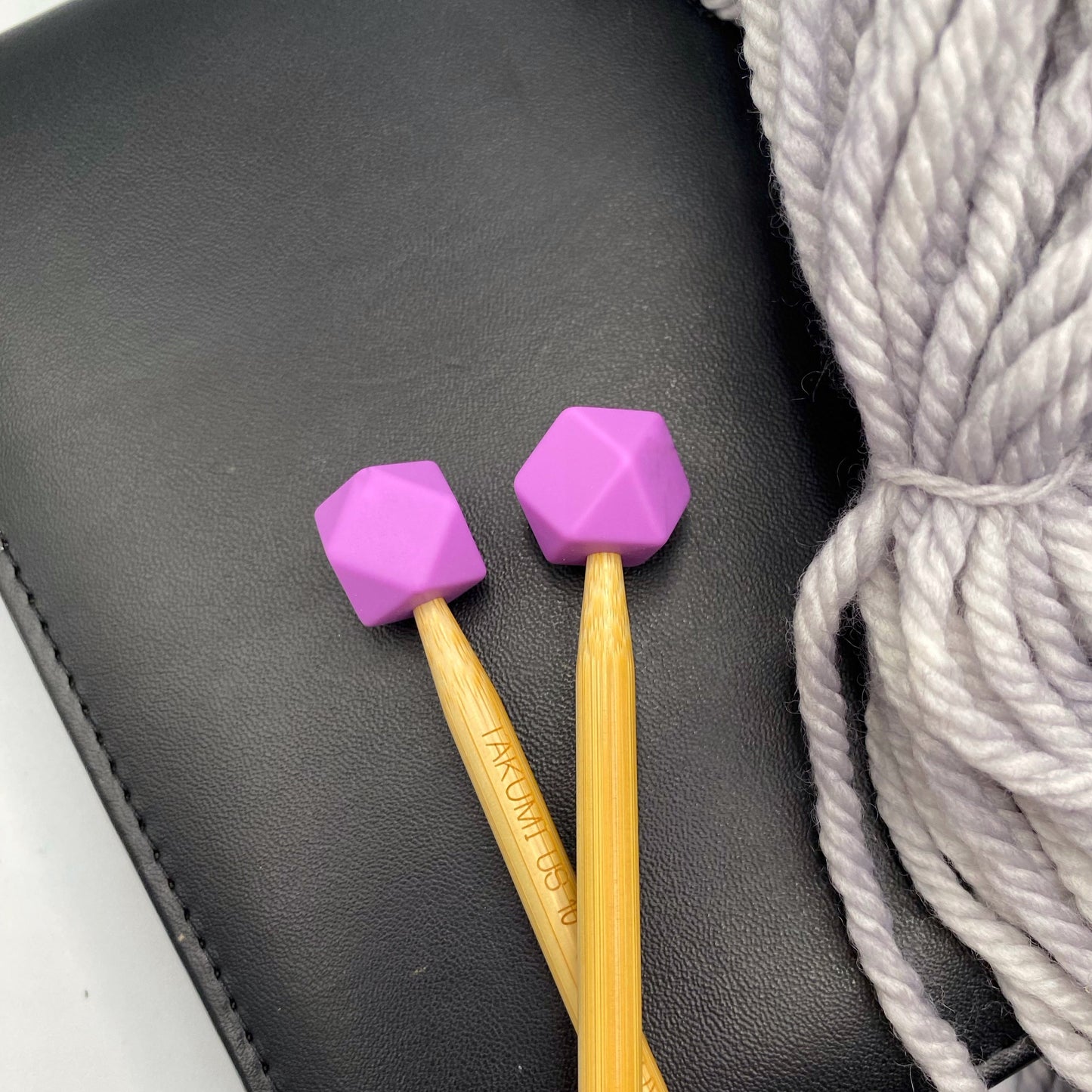 a set of knitting needles adorned with orchid (purple) hexagon point protectors, laid on top of a spread of our Everyday Bulky in Urban.